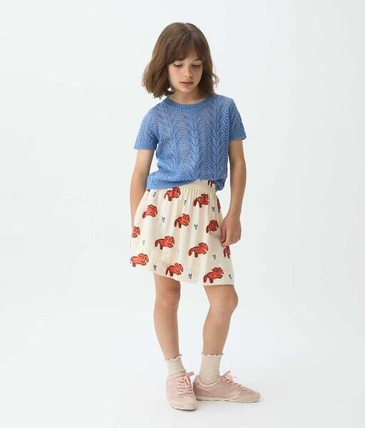 Meisje draagt blauwe gebreide trui met witte rok met rode olifantenprint en roze sneakers