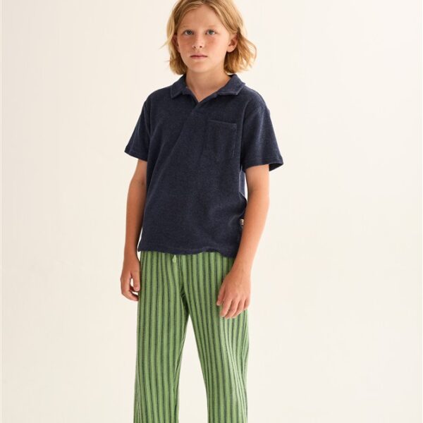Jongen draagt donkerblauw poloshirt en groen gestreepte broek met witte sneakers