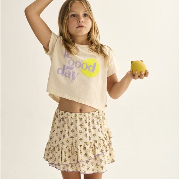 Meisje met twee groene appels draagt crop top met tekst 'good day' en gebloemde rok op witte achtergrond