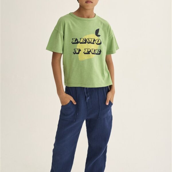 Jongen in groen t-shirt met citroenenprint en blauwe broek op witte achtergrond