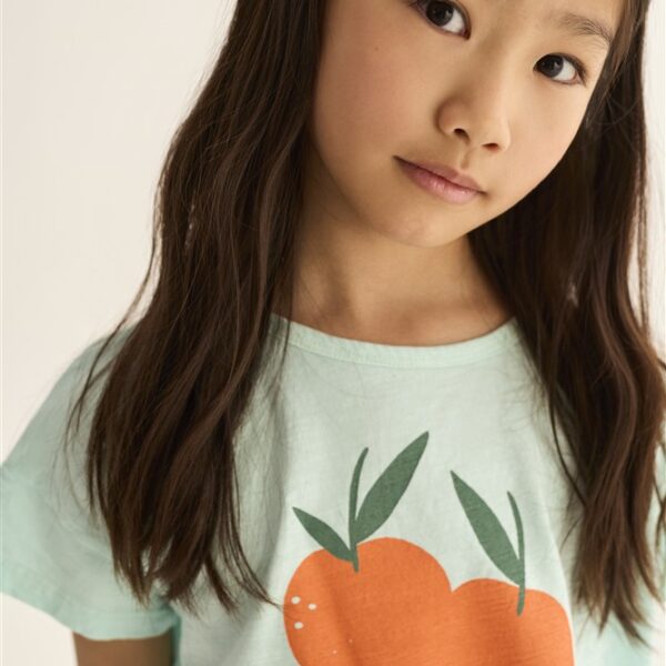 Jong meisje met lang bruin haar draagt mintgroen T-shirt met sinaasappel print en tekst Clementine
