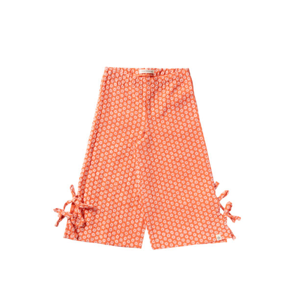 Oranje kinderbroek met wit bloemenpatroon en strikjes aan de pijpen